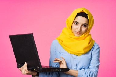 Sarı tesettürlü neşeli Müslüman kadın dizüstü bilgisayar öğreniyor.