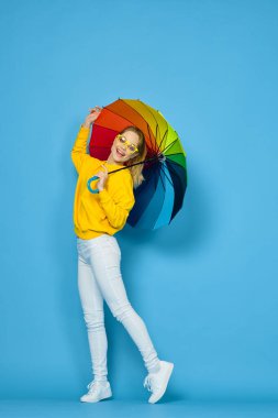 Sarı kazaklı, renkli şemsiyeli kadın gökkuşağı rengi pozlar veriyor.