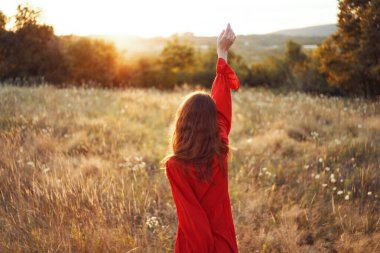 Kırmızılı kadın, tarlada ellerini kaldırıp poz veriyor.