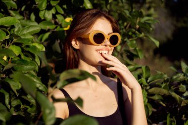 Güneş gözlüğü takan neşeli kadın yeşil yapraklar doğada yaz pozu veriyor