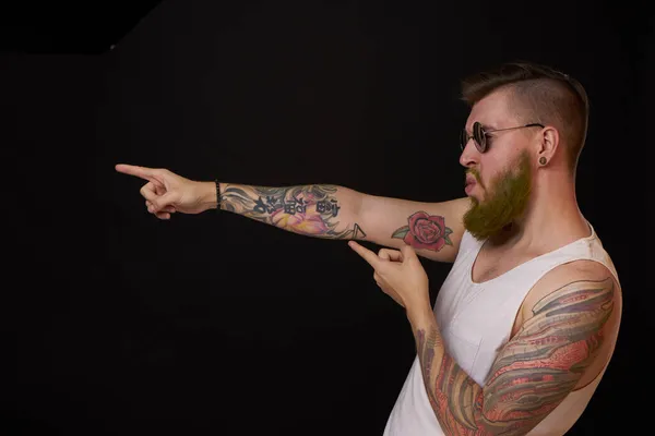 Hombre barbudo en camiseta blanca con tatuajes en sus brazos posando bravucón — Foto de Stock
