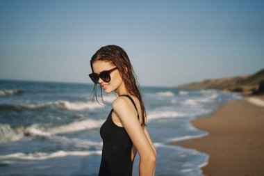 Siyah mayo giymiş güzel bir kadın kumsalda güneşleniyor.