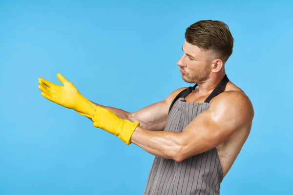 Man in schort met opgepompt lichaam rubber handschoenen schoonmaken blauwe achtergrond — Stockfoto