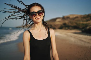 Siyah mayo giymiş bir kadın, kumlu sahilde yürüyor. Tropiklerde.