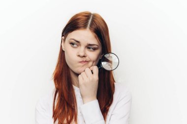 Neşeli kızıl saçlı kadın yüzünün yanında büyüteç tutuyor.