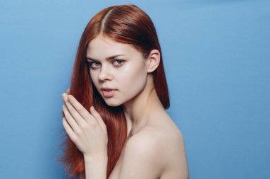 Çıplak omuzlu bir kadın. Kızıl saçlı, mavi arkaplan.