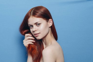 Çıplak omuzlu bir kadın. Kızıl saçlı, mavi arkaplan.