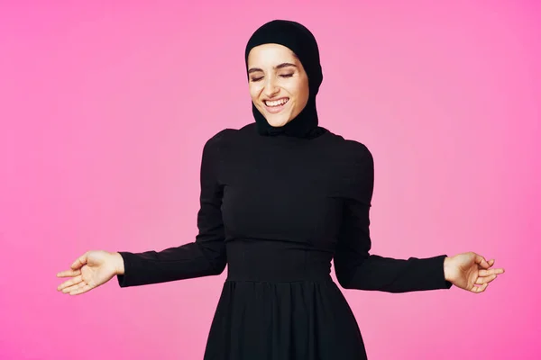 穿着黑色头巾的快乐的穆斯林女人，摆出时髦的粉色背景 — 图库照片