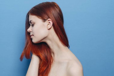 Çıplak omuzlu bir kadın. Kızıl saçlı, mavi arkaplan.