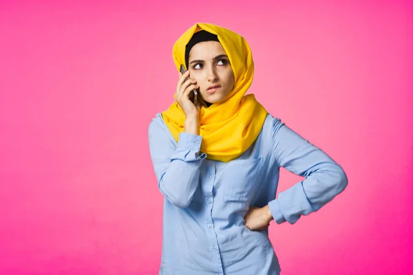 Moslim vrouw in gele hijab praten op de telefoon roze technologie achtergrond — Stockfoto