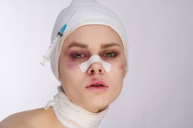 Yüzü bandajlı duygusal bir kadın. Şırınga arka planda duruyor.