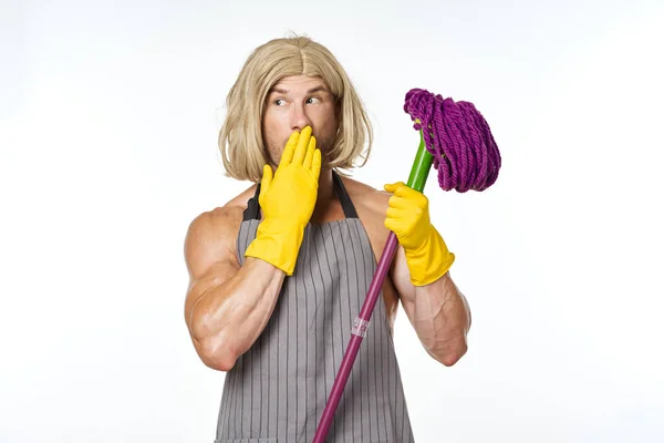 Muscular man in apron with a mop in a womans wig — Stock Photo, Image