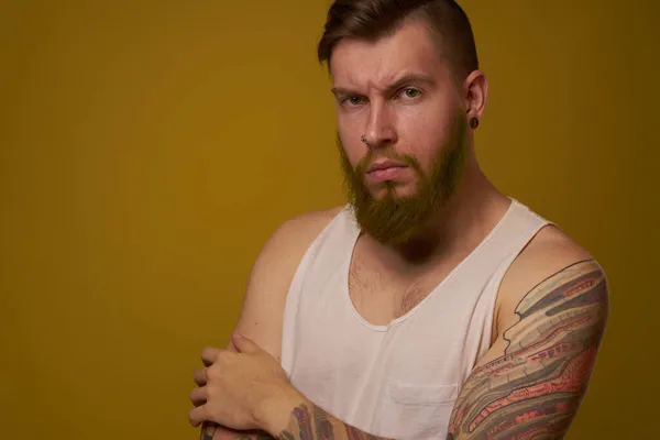 Бородатый мужчина в белой футболке с татуировками на руках, позирующий серьезным взглядом — стоковое фото