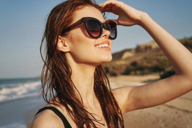 Güneş ışığı adasında, güneş gözlüklü, mayolu neşeli bir kadın.