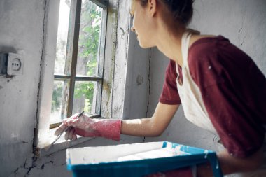 Kadın ressam pencerenin iç tarafında ev onarımı yapıyor.