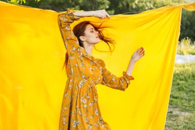 Sarı elbiseli gülümseyen kadın doğaya sarılık pozu veriyor.