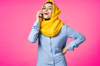 Sarı tesettürlü müslüman kadın telefon teknolojisi pembe arka planda konuşuyor.