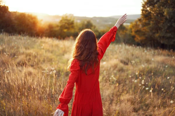 Mulher em vestido vermelho no campo com as mãos levantadas posando — Fotografia de Stock