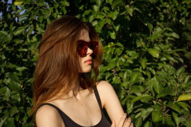 Yeşil yaprakların arkasında poz veren çekici bir kadın.