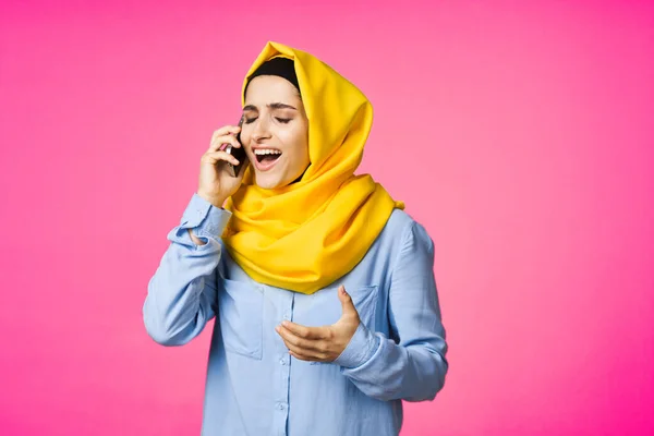 Mujer musulmana en hijab amarillo hablando sobre la tecnología del teléfono de fondo rosa —  Fotos de Stock