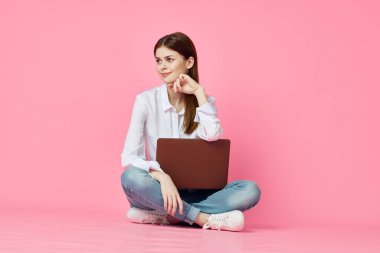 Dizüstü bilgisayarı olan bir kadın internet alışverişinde pembe arka planda oturuyor.