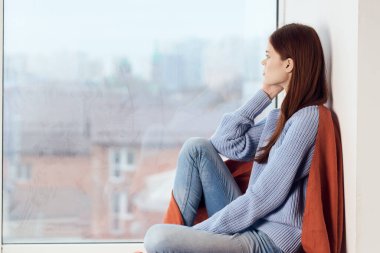 Hüzünlü yüzü olan kadın elinde ekoseyle pencerenin kenarında oturuyor.