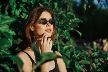 Güneş gözlüklü ve yeşil yapraklı neşeli moda kadın Rus yazı