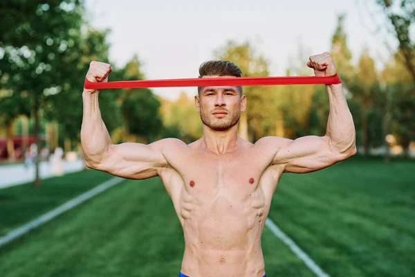 Atletische man met een opgepompt lichaam in het park oefening fitness — Stockfoto