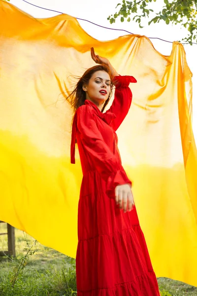 Vacker kvinna i röd klänning gult tyg på naturen bakgrund — Stockfoto