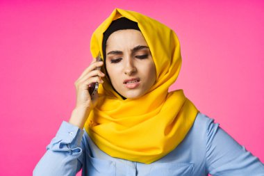 Sarı tesettürlü müslüman kadın telefonda pembe teknolojiyle konuşuyor.