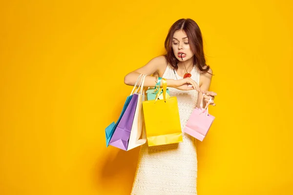Leende kvinna med förpackningar i händerna Shopaholic gul bakgrund — Stockfoto