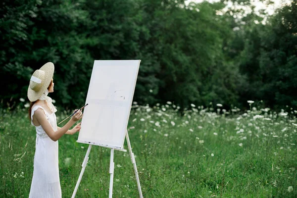 Žena v bílých šatech na poli s květinami maluje obraz — Stock fotografie