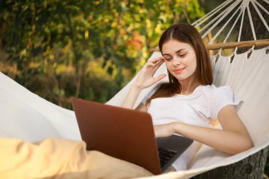 Dizüstü bilgisayarı olan kadın hamakta serbest seyahat ediyor.