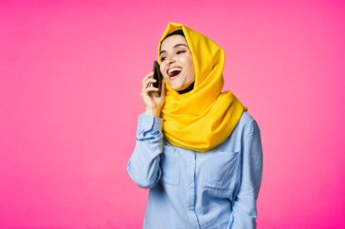 Sarı tesettürlü müslüman kadın telefon teknolojisi pembe arka planda konuşuyor.
