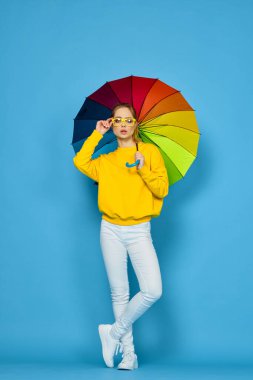 Sarı kazaklı, renkli şemsiyeli kadın gökkuşağı rengi pozlar veriyor.