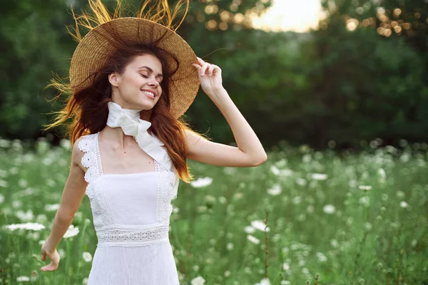 Bella donna in un cappello in un campo con fiori a piedi — Foto Stock