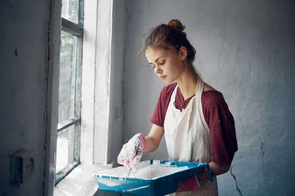 Woman in aprons paints window home renovation interior — Stock Photo, Image