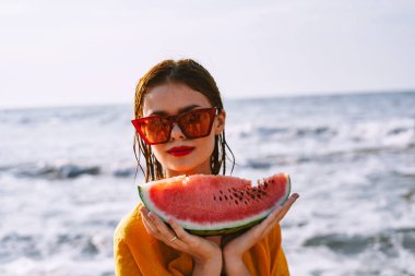 Okyanus kıyısındaki sahilde karpuz yiyen bir kadın.