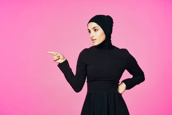 穿着黑色头巾的快乐的穆斯林女人，摆出时髦的粉色背景 — 图库照片