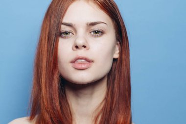 Çıplak omuzlu çekici bir kadın. Kızıl, yakın plan, mavi arka plan.