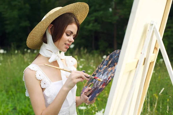 Bonita mujer en sombrero artista pinta un cuadro en la pintura de la naturaleza —  Fotos de Stock