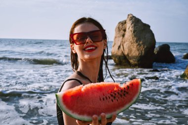 Ellerinde karpuz olan siyah mayo giymiş güzel bir kadın.