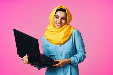 Laptop teknolojisi öğrencisi pembe geçmişli sarı tesettürlü müslüman kadın.