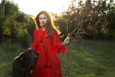 Açık havada kırmızı elbiseli güzel bir kadın ve siyah bir köpek arkadaşlığı.