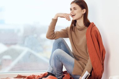 Pencerenin yanında elinde bir fincan kahve olan bir kadın.