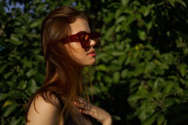 Yeşil yaprakların arkasında poz veren çekici bir kadın.