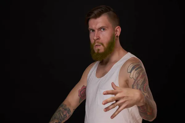 Homme barbu avec des tatouages sur les bras gesticulant avec ses mains fond sombre — Photo