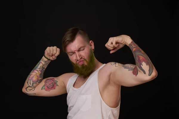 Homme barbu avec des tatouages sur les bras gesticulant avec ses mains fond sombre — Photo