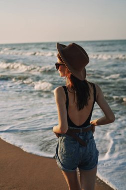 Kumsalda yürüyen bir kadın, tatil güneşinde seyahat ediyor.