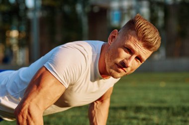 Atletik adam sabah halterlerle antrenman yapıyor. Park.